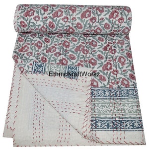May include: A white cotton kantha quilt with a floral print in shades of pink and green. The quilt has a border with a blue and green floral pattern. The quilt is folded in half and the edges are stitched with red thread. "EthnicKraftWorkz" is printed on the quilt.