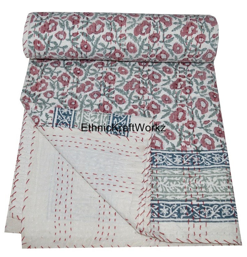 May include: A white cotton kantha quilt with a floral print in shades of pink and green. The quilt has a border with a blue and green floral pattern. The quilt is folded in half and the edges are stitched with red thread. "EthnicKraftWorkz" is printed on the quilt.