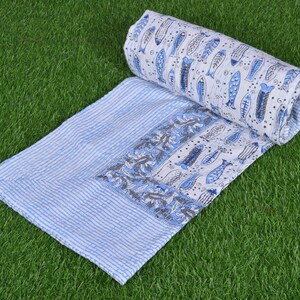 May include: A white and blue cotton quilt with a pattern of fish and floral designs. The quilt is rolled up and has a striped border.