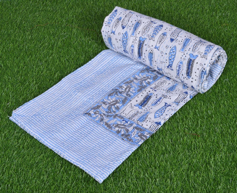 May include: A white and blue cotton quilt with a pattern of fish and floral designs. The quilt is rolled up and has a striped border.