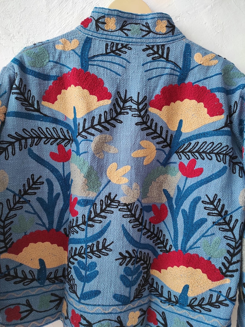 Peut inclure: Veste bleu clair avec broderie florale d&eacute;taill&eacute;e. Le motif pr&eacute;sente des fleurs rouges, beiges et jaunes, ainsi que des feuilles et des tiges vertes et noires. Gros plan sur la couture complexe.