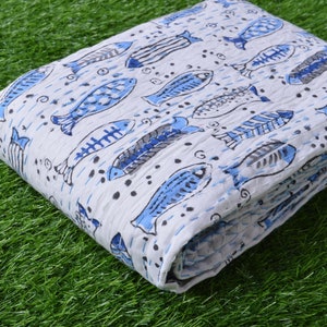 May include: White cotton fabric with a blue fish print. The fabric is folded and has a textured surface.