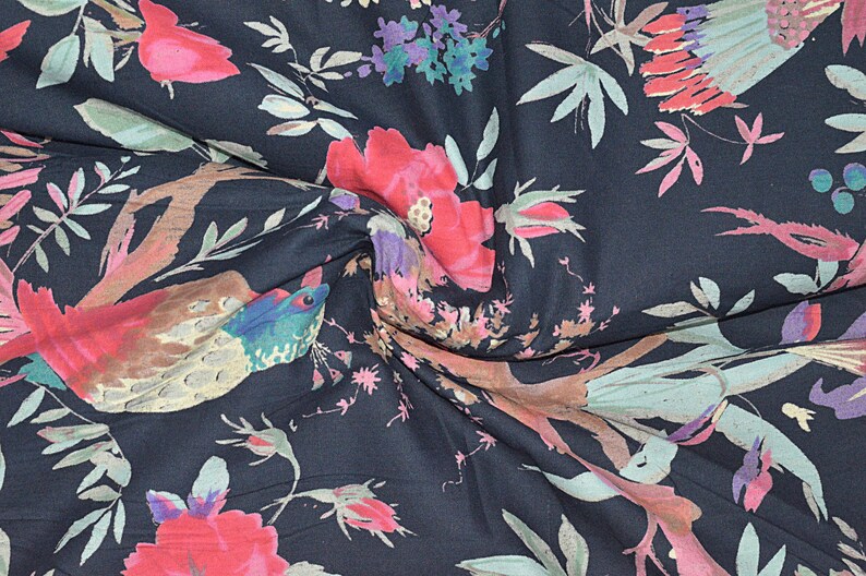 May include: A dark blue fabric with a floral print featuring pink and red flowers, green leaves, and brown birds. The fabric has a soft, flowing texture.