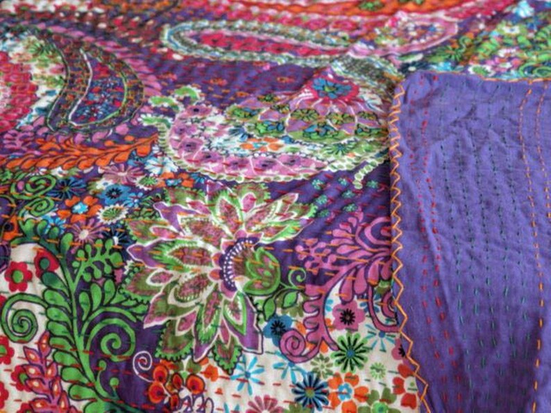 Puede incluir: Una colcha kantha colorida con un patr&oacute;n de paisley en tonos de morado, rosa, verde, naranja y azul. La colcha est&aacute; cosida a mano con una puntada corrida y tiene un respaldo morado.