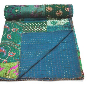 May include: A patchwork quilt with a teal blue background and green, pink, and white floral patterns. The quilt is made of various fabrics and is hand-stitched with intricate details.