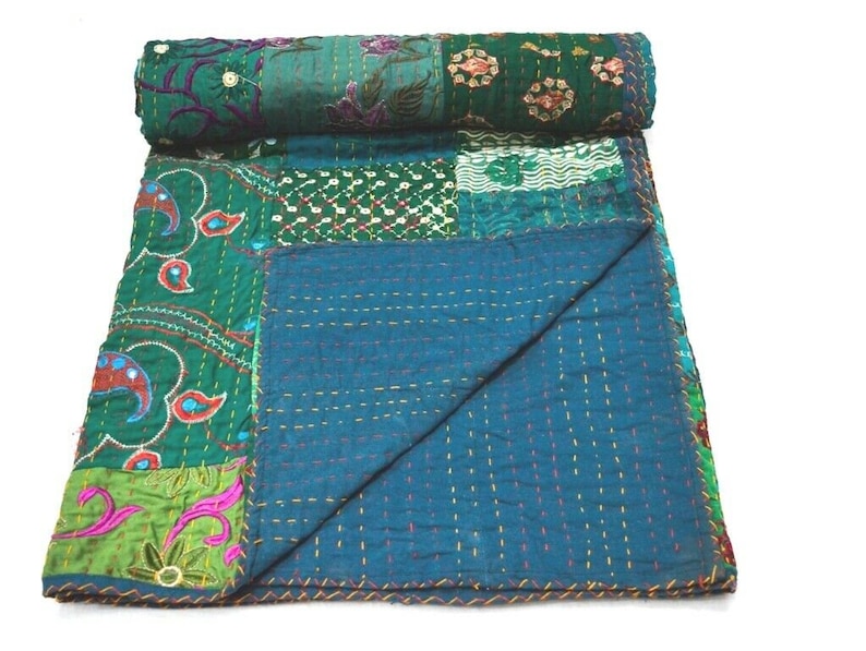 May include: A patchwork quilt with a teal blue background and green, pink, and white floral patterns. The quilt is made of various fabrics and is hand-stitched with intricate details.