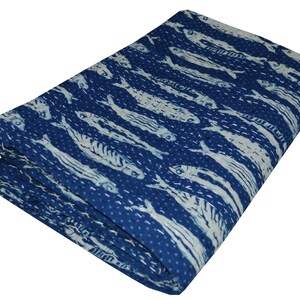 May include: A blue kantha quilt with a white fish pattern. The quilt is folded and has a textured surface.