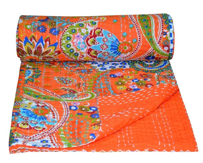 Puede incluir: Colcha kantha naranja con estampado paisley y detalles florales. La colcha est&aacute; doblada por la mitad y enrollada.