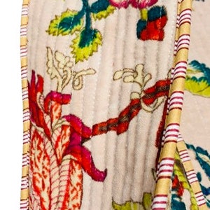 May include: A close-up of a cream-colored fabric with a floral pattern. The fabric has a quilted texture and is trimmed with a yellow and red striped ribbon.