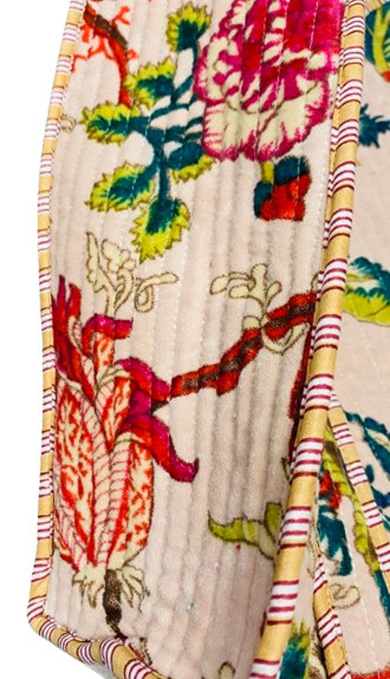 May include: A close-up of a cream-colored fabric with a floral pattern. The fabric has a quilted texture and is trimmed with a yellow and red striped ribbon.