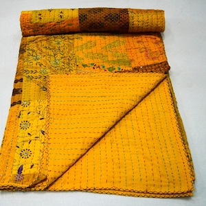 Könnte beinhalten: Eine gelbe Kantha-Steppdecke mit aufwendigen Stickereien und Patchwork-Details. Die Decke ist in der Hälfte gefaltet und hat einen Fransenrand.