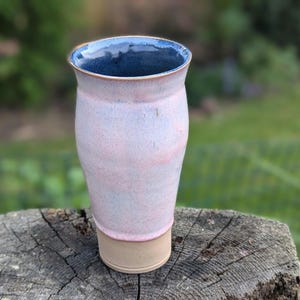 May include: A ceramic mug with a pink and blue glaze. The mug has a wide base and a slightly flared top.