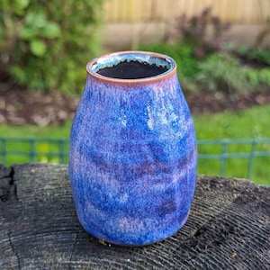 May include: A small, blue and purple ceramic vase with a speckled glaze. The vase has a rounded shape and a wide opening.
