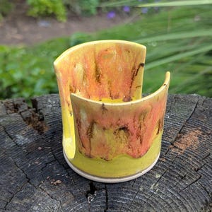 May include: A ceramic sponge holder with a distinctive design. The holder has a yellow, orange, and brown colour scheme with a glossy finish. The curved shape is designed to hold a sponge, adding a touch of artistry to the kitchen. Measures approximately 10 cm in height.
