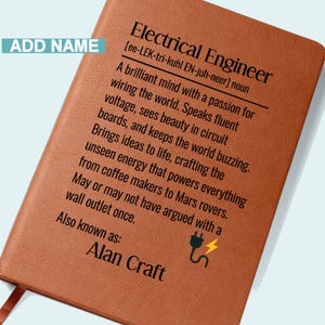 May include: A brown leather-bound notebook with the title "Electrical Engineer" and a definition. The text includes a name, "Alan Craft", and a graphic of a plug with lightning. The notebook has a ribbon bookmark.