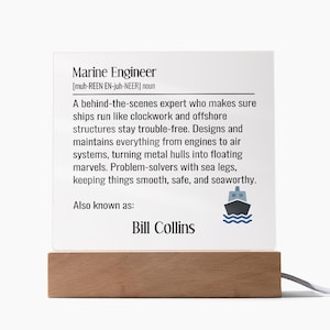 Peut inclure: Lampe décorative avec une base en bois et un panneau blanc. Le panneau affiche la définition de "Ingénieur maritime" avec le nom "Bill Collins" en dessous. Un petit graphique de navire est également inclus.