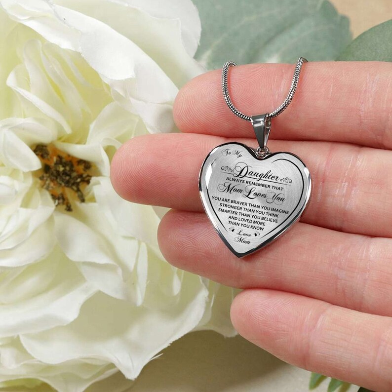 Pode incluir: Colar de prata em forma de cora&ccedil;&atilde;o com uma mensagem que diz "To My Daughter Always Remember That Mom Loves You You Are Braver Than You Imagine Stronger Than You Think Smarter Than You Believe And Loved More Than You Know Love Mom".
