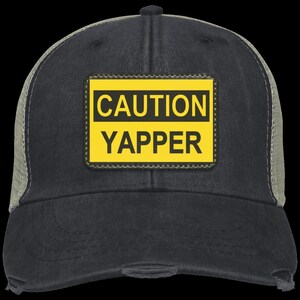 May include: A black and gray trucker hat with a yellow patch that says "CAUTION YAPPER" in black letters.