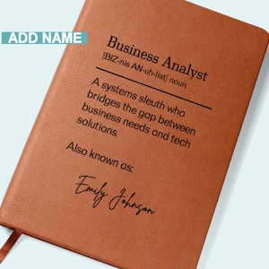 May include: A tan faux-leather notebook featuring the words "Business Analyst" and a definition. The notebook includes the name "Emily Johnson" and the words "Add Name" in a blue box. A ribbon bookmark is visible.