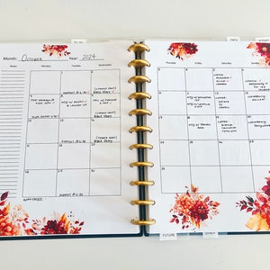 May include: A monthly planner with a fall theme. The planner has a white background with black grid lines and a floral design with red, orange, and yellow flowers. The month of October is written at the top of the page, along with the year 2024. The planner is open to the week of October 14th through the 20th. The days of the week are listed across the top of the page, and the dates are listed down the side. There are handwritten notes in the boxes for each day.