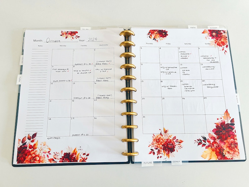 May include: A monthly planner with a fall theme. The planner has a white background with black grid lines and a floral design with red, orange, and yellow flowers. The month of October is written at the top of the page, along with the year 2024. The planner is open to the week of October 14th through the 20th. The days of the week are listed across the top of the page, and the dates are listed down the side. There are handwritten notes in the boxes for each day.