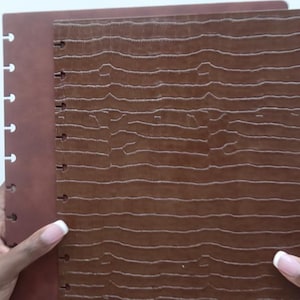 Peut inclure: Deux journaux reliés en cuir marron avec une couverture texturée. Le journal de droite a un motif gaufré plus prononcé.