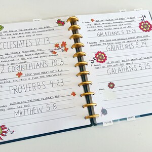 May include: A weekly planner with a blue cover and white pages. The pages are filled with handwritten notes and bible verses. The planner has a gold coil binding and is decorated with colorful floral stickers.