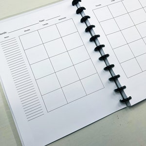 May include: A white planner with a black coil binding. The planner has a monthly calendar layout with spaces for notes and a section for the year and month.