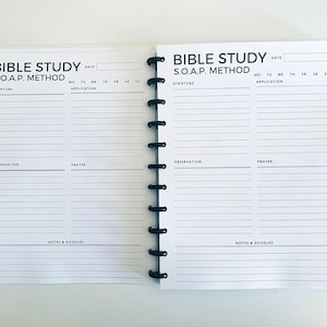 Op de afbeelding: Een wit, spiraalgebonden notitieboek met een zwarte omslag. De omslag heeft de tekst "Bible Study S.O.A.P. Method" en een lege ruimte voor de datum. Het notitieboek is verdeeld in secties voor "Scripture", "Observation", "Application" en "Prayer".