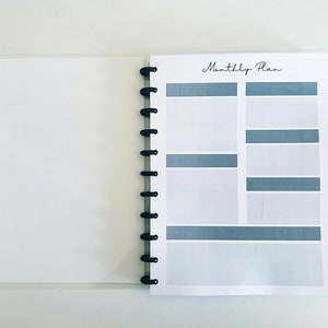 May include: A white planner with a black spiral binding. The cover has the text "Monthly Plan" printed in black.