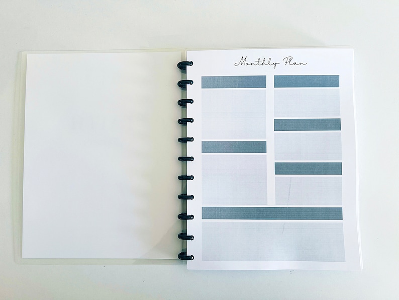 May include: A white planner with a black spiral binding. The cover has the text "Monthly Plan" printed in black.