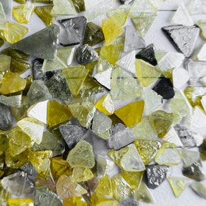 Op de afbeelding: Een close-up van een verzameling kleine, driehoekige, gefacetteerde edelstenen. De edelstenen zijn een mix van gele, groene en grijze kleuren.