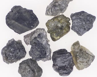 May include: A selection of raw gemstones in shades of grey, black, and pale yellow. The uncut stones have irregular shapes and a textured surface, set against a white backdrop. These crystals are suitable for jewellery making or collecting.