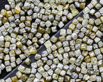 Puede incluir: Una imagen de primer plano de una gran cantidad de pequeños diamantes en bruto grises y amarillos. Los diamantes están dispersos sobre una superficie negra.