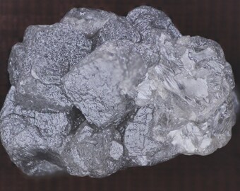 Puede incluir: Un grupo de cristales rugosos, grises y translúcidos. Los cristales están agrupados en una forma rugosa e irregular.