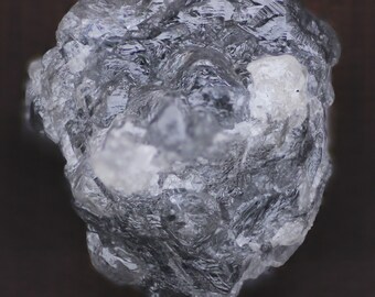 Puede incluir: Un cristal áspero, gris y transparente con una sección blanca opaca. El cristal tiene una superficie rugosa y desigual.
