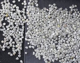 May include: A close-up of a pile of small, white, rough diamonds. The diamonds are scattered on a black surface and in a small, black tray.