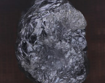 Puede incluir: Un diamante grande, claro, facetado, de corte tosco con un tono gris. El diamante tiene muchas facetas y parece ser un cristal natural.