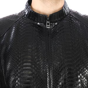 Op de afbeelding: Een zwart leren jack met een slangenhuidpatroon. Het jack heeft een ritssluiting en een opstaande kraag.