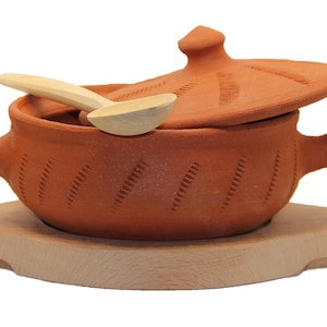 Peut inclure: Un pot en terre cuite avec un couvercle et une cuillère en bois. Le pot a un motif décoratif et repose sur une base en bois.