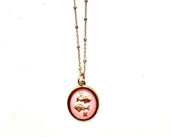 May include: Gold chain necklace with a pink circular pendant featuring a gold zodiac symbol of two fish.