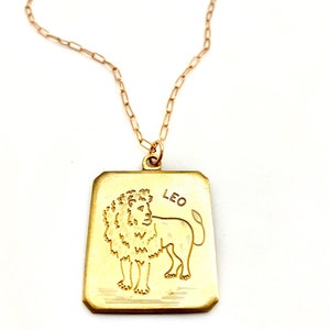 May include: Gold chain necklace with a gold rectangular pendant featuring a line drawing of a lion and the word "LEO".