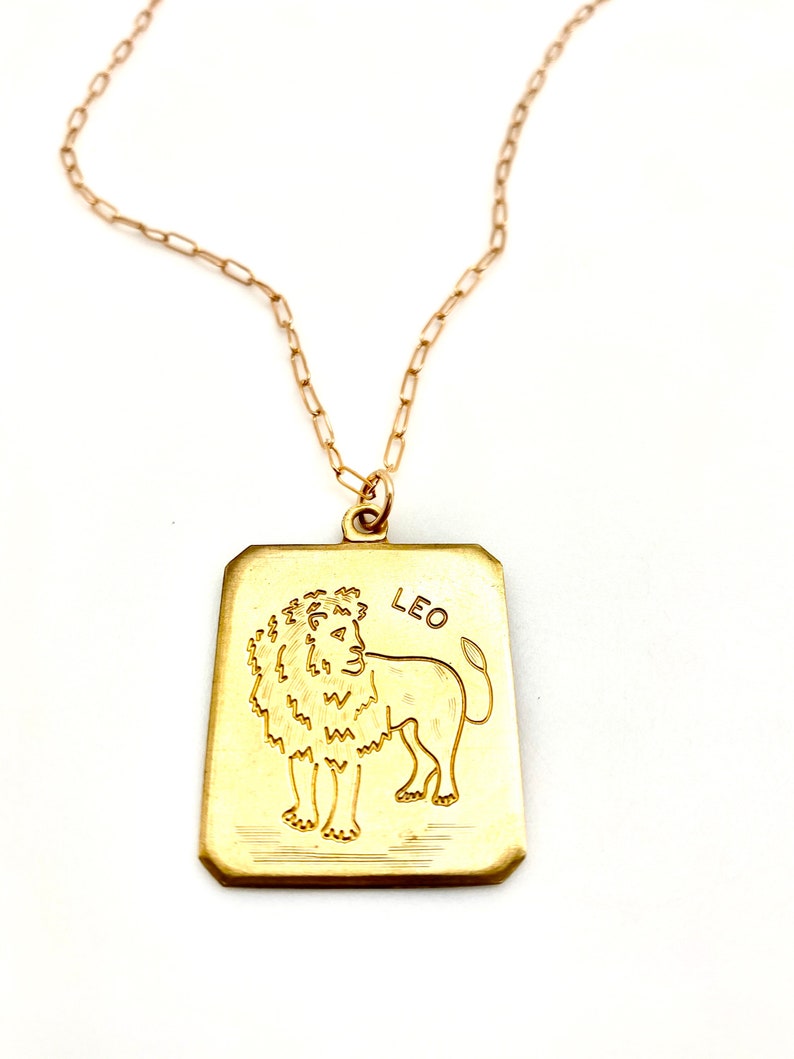 May include: Gold chain necklace with a gold rectangular pendant featuring a line drawing of a lion and the word "LEO".