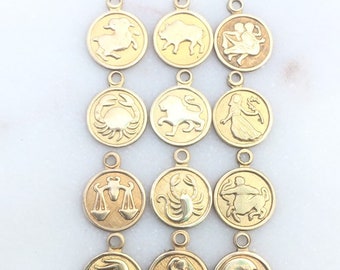 May include: Gold-colored zodiac charm pendants. Each pendant features a different zodiac symbol, including a ram, bull, twins, crab, lion, maiden, scales, scorpion, archer, water bearer, and fish. The pendants are round with a loop at the top.