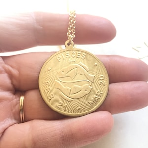 May include: Gold necklace with a round pendant featuring the Pisces zodiac symbol and the dates "Feb 21 - Mar 20".
