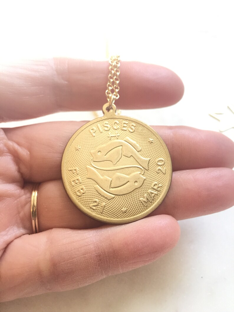 May include: Gold necklace with a round pendant featuring the Pisces zodiac symbol and the dates "Feb 21 - Mar 20".