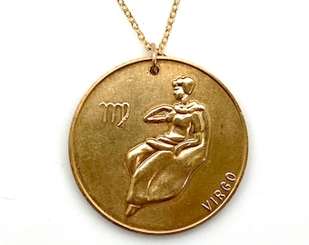 May include: Gold necklace with a round pendant featuring the Virgo zodiac sign and the word "VIRGO" inscribed on the bottom.