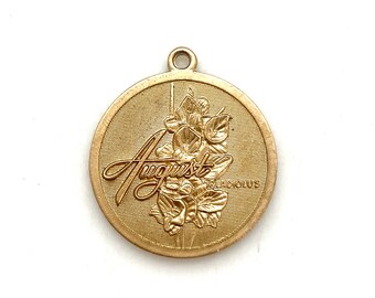 May include: A gold-colored metal charm with the word "August" and a floral design. The flower is a gladiolus.