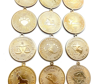 May include: Twelve gold-colored metal zodiac charms with the astrological signs and dates. The charms are round and have a raised design.