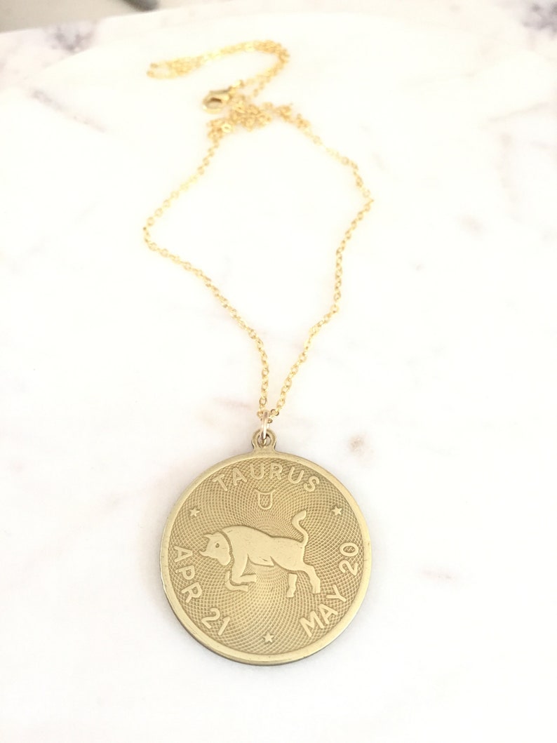 May include: Gold chain necklace with a round pendant featuring the Taurus zodiac sign, a bull, with the dates April 21 to May 20.
